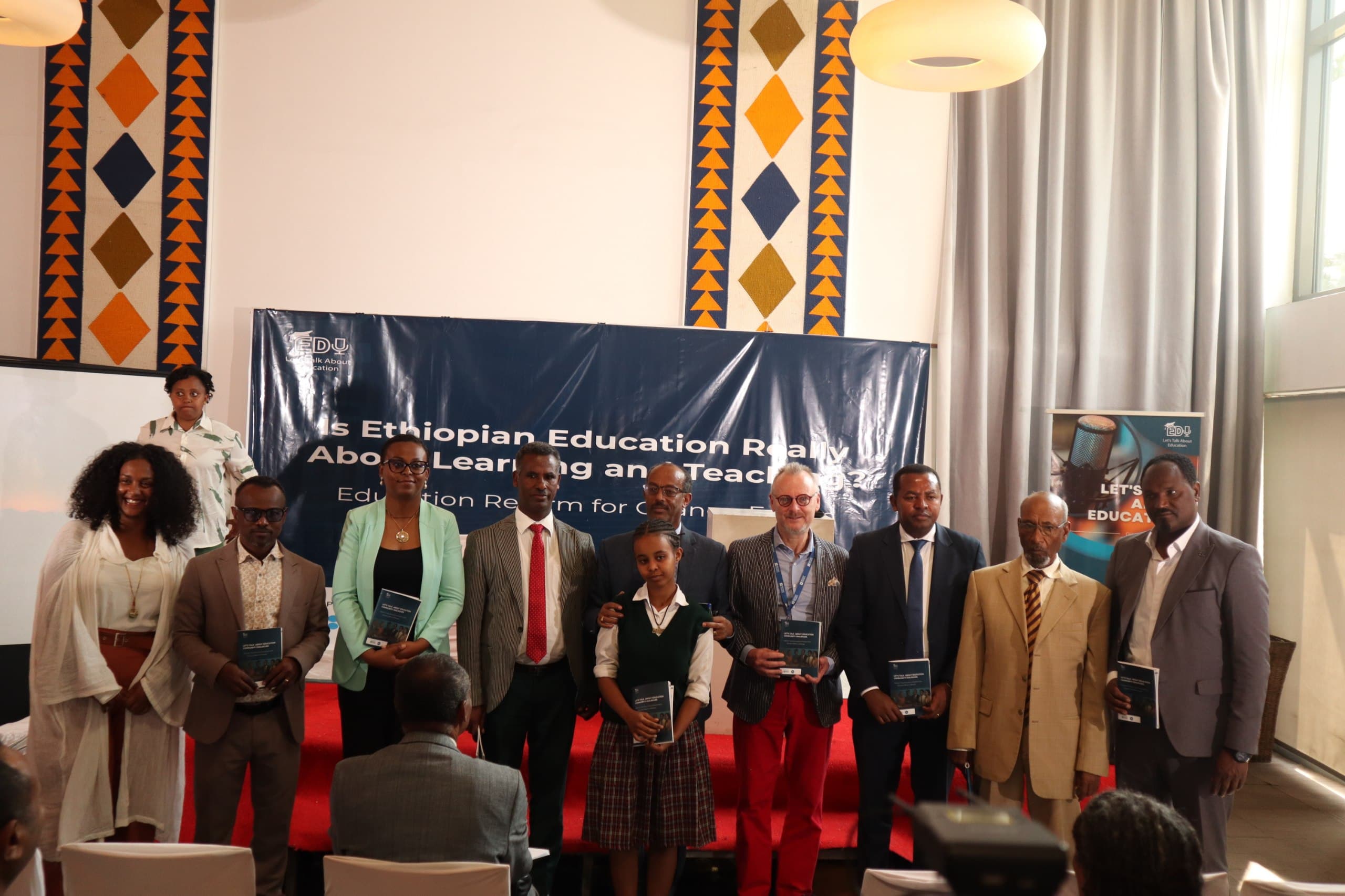 Speakers on stage holding copies of the Let's Talk About Education report