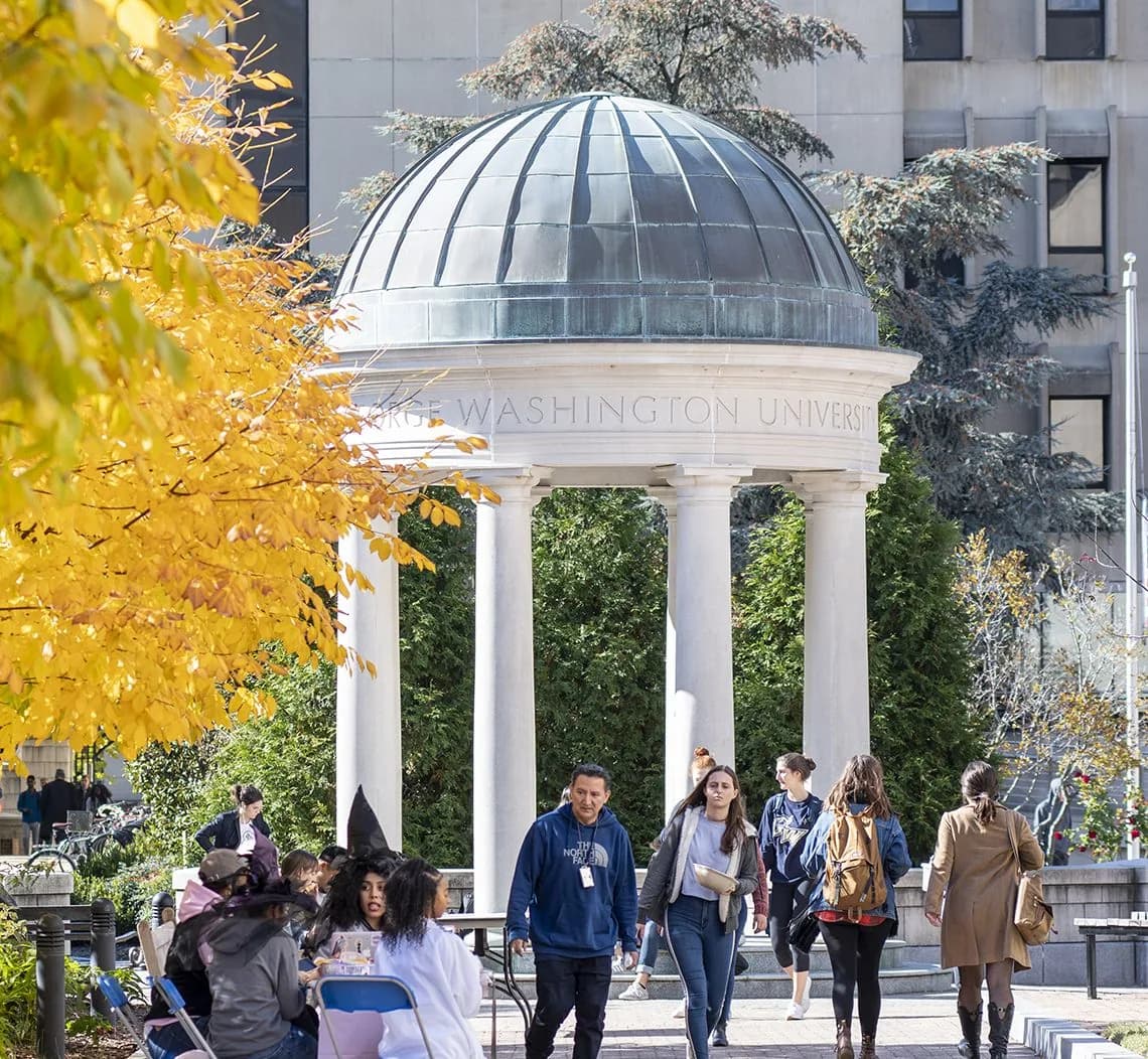 Students walking past the domed George Washington University monument on campus in autumn